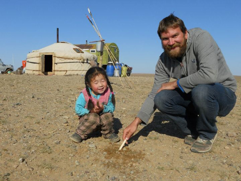 Peter Berg visiting with a young friend in the Gobi Desert of Mongolia. Thunderbird Atlatl darts are in the background near the yurt or ger.