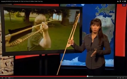 Screenshot of the Atlatl Clue. The presenter is holding our Catatonk Atlatl and a Dart. In the video clue, Bob is casting a dart with our Wyalusing Atlatl